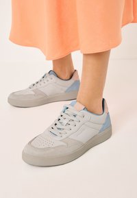 Adidași gri deschis cu accente albastre și roz, având o suprafață texturată, vârf rotunjit și design cu șireturi. Materiale din suede moale și piele netedă.