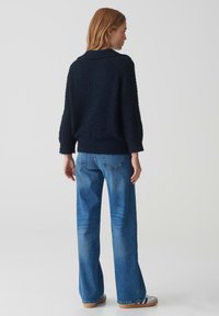 Pull en maille texturée bleu marine avec col, associé à un jean bleu clair à coupe ample avec poches arrière et un léger dégradé.