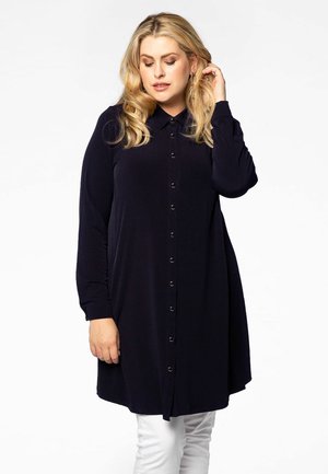 Tunique bleu marine à boutons, avec une texture lisse, des manches longues et une patte de boutonnage devant. Tissu doux et coupe décontractée.