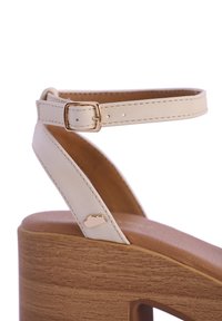 Sandalia de tacón alto color beige con plataforma de madera, correa ajustable en el tobillo con hebilla dorada y un pequeño detalle en forma de nube en la correa.