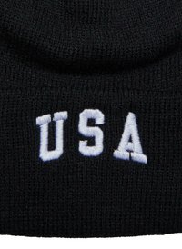 Černá pletená čepice s bílým vyšitým textem "USA" umístěným vpředu. Měkká textura a těsné přiléhávání.