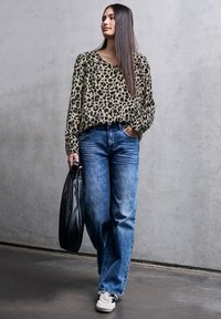 Blusa a stampa leopardata con scollo a V, maniche lunghe e polsini. Jeans in denim azzurro chiaro e sneaker bianche. Borsa tote nera. Texture lisce.