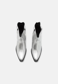 Botas de tobillo plateadas con punta afilada y acabado brillante. Presentan paneles laterales elásticos y un diseño de parte superior texturizada. Suela negra.