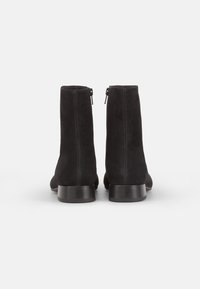 Bottines à cheville en daim noir avec une texture lisse, un bout rond et des coutures contrastées ; elles possèdent une fermeture éclair latérale et un talon carré.