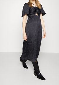 Vestido negro, de longitud hasta la rodilla, con mangas cortas y vaporosas y una apertura en forma de llave en el frente; cuenta con tela texturada y un ajuste relajado. Combinado con botas negras.