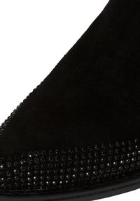 Stivale alla caviglia in suede nero con punta appuntita, caratterizzato da una fila di perline nere lungo il bordo superiore per un tocco decorativo. Texture liscia.