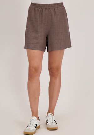 Bruine, gestructureerde shorts met een elastische tailleband en zijzakken, gecombineerd met witte sneakers met zwarte accenten.