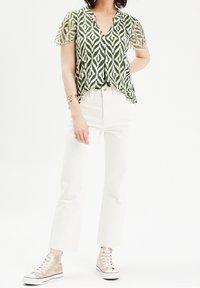 Grøn og hvid mønstrede t-shirt med korte ærmer, v-hals design, parret med hvide højtaljede jeans og beige høj-top sneakers.