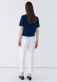 Marineblå crop top med korta ärmar, parat med vita slim-fit byxor och svarta platta skor. Minimalistisk design med rena linjer och inga synliga mönster.