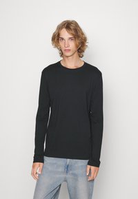 Langærmet sort t-shirt i blødt stof med rund halsudskæring, tætsiddende silhuet og minimalt design. Kombineret med lyseblå denimjeans.