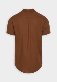 Camicia a maniche corte in tessuto marrone, con colletto, dettaglio della piega sul retro, orlo curvo e un accento di bottone sul lato.