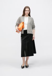 Cardigan grigio, camicia bianca, gonna nera con trama, scarpe nere, che tiene una borsa clutch geometrica arancione. Design semplice con accenti moderni.