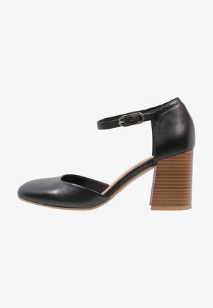 Escarpins noirs en cuir avec une bride au niveau de la cheville, un bout rond et un talon en bois texturé. Présente un design minimaliste et une finition lisse.