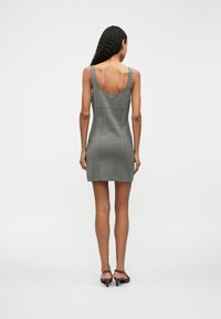 Rochie gri fără mâneci, cu spatele decupat, siluetă ajustată, până la genunchi, realizată dintr-un material texturat. Asortată cu pantofi cu toc maro.
