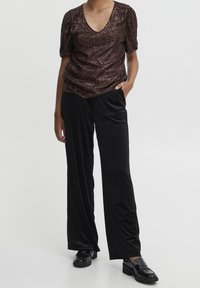 Bronze paljetterad topp med V-ringning och korta puffärmar. Matchas med svarta, löst sittande velourbyxor och glänsande svarta loafers.