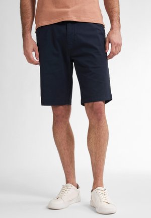 Pantaloni corti blu navy in cotone con una vestibilità comoda, dotati di tasche laterali e una texture liscia, abbinati a sneakers bianche su uno sfondo chiaro.