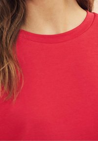 Red cotton t-shirt featuring a classic crew neck design. The texture appears smooth and soft, with visible stitching around the neckline.