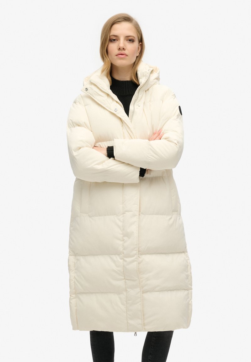Polstret knælang frakke i off-white, med højt krave, lynlås foran, to sidelommer og elastiske manchetter. Glat tekstur, letvægtsdesign.