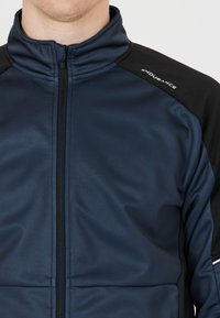 Mörkblå sportjacka med hög krage, svarta axelinsatser och central dragkedja. Har en slät yta och varumärkeslogotyp.