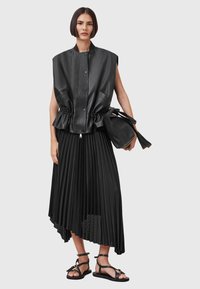 Black leather sleeveless top with a gathered waist, paired with a flowing black pleated skirt featuring an asymmetric hem and strappy sandals.