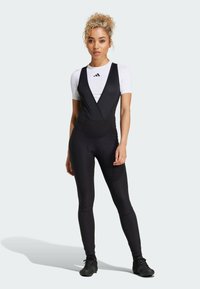 Zwarte sportbodysuit met een gestructureerde, wikkelstijl voorkant, gecombineerd met een witte top met korte mouwen. Fittende benen en slank ontwerp.