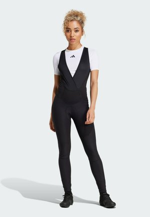Sort atletisk bodysuit med en struktureret, omslagslignende forside, kombineret med en hvid kortærmet top. Stramme ben og slankt design.