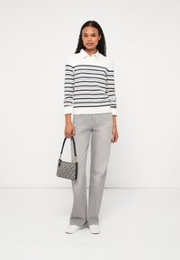 Stripete genser i hvit og marineblå, grå vid bukse og en svart og kremmønstret veske med gullhardware. Hvite sneakers.