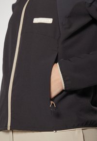 Veste noire avec une fermeture �éclair et des accents de couleur claire. Dotée d'une poche avec un tirette de fermeture éclair, des poignets froncés et une coupe confortable.