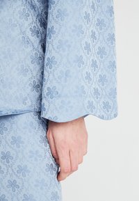Světle modrá látka s květinovým vzorem a texturovanými akcenty. Rukáv má hladký okraj, což zvyšuje celkový design.