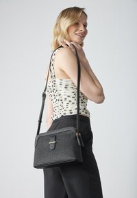 Schwarze, strukturierte Handtasche in rechteckiger Form, mit einem goldenen Akzent und einem langen, verstellbaren Schultergurt, der quer über den Körper getragen wird.