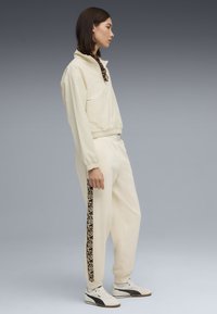 Krämfärgad tröja med hög krage, kombinerad med matchande joggers med leopardmönstrad sidostripa och vita sneakers.