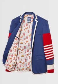 Veste bleue avec bordure blanche et manches rayées rouges, ouverte pour montrer la doublure ornée de motifs de pop-corn, hot-dogs et gobelets de soda.