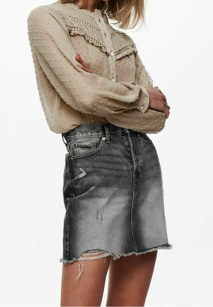Beige Bluse mit strukturierten Punkten und Spitzendetails, kombiniert mit einem ausgewaschenen schwarzen Denim-Rock mit fransigem Saum und sichtbaren Used-Effekten.