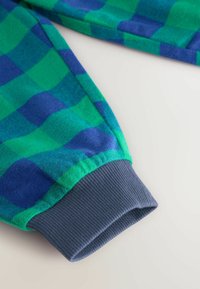 Tela a cuadros en verde y azul con una textura suave, que presenta un puño gris acanalado en el extremo. El diseño tiene patrones de cuadros grandes.