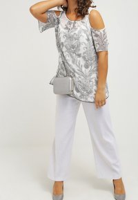 Hopeahuivilla ja valkoinen kukkakuosiset tunikapaita, jossa on avonaiset olkapäät, yhdistettynä valkoisiin leveälahkeisiin housuihin ja pieneen hopea käsilaukkuun. Hopeiset korkokengät viimeistelevät asun.