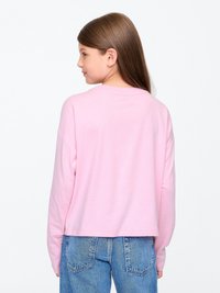 Camisa de algodão rosa de manga longa com um decote redondo, corte descontraído e bainha cropped, combinada com jeans de cintura alta em azul claro.