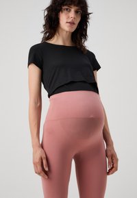 Top nero a maniche corte abbinato a leggings a vita alta rosa chiaro, caratterizzati da una texture liscia e un tessuto elastico per il massimo comfort.