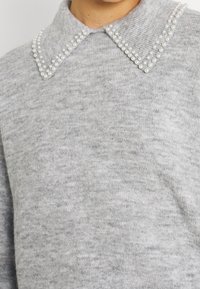 Pull gris en maille avec col pointu orné de deux rangées de petites perles blanches le long des bords.