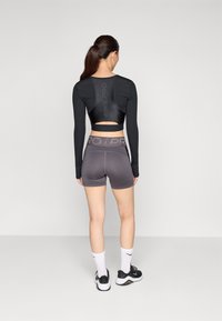 Crna majica dugih rukava s izrezom na leđima; sivi šorts s pojasom "NIKE PRO"; upotpunjeno bijelim čarapama i crnim sportskim tenisicama.