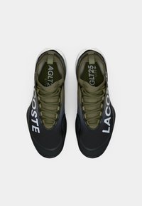 Crne i maslinasto zelene tenisice s teksturiranim materijalom, prednjim vezanjem, gumenim potplatom i velikim bijelim logom "LACOSTE" sa strane.