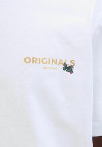 Hvid bomulds t-shirt med guld "ORIGINALS" tekst og en sommerfugl samt blomsterbroderi, samt "EST.1990" trykt nedenfor.