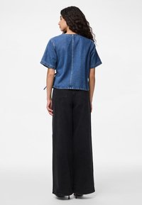Top in denim con maniche corte, design corto e dettaglio della cucitura sul retro. Abbinato a pantaloni neri a gamba larga, dotati di taschini sul retro.