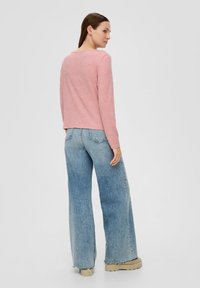 Helles rosa Langarmoberteil mit rundem Halsausschnitt, kombiniert mit weiten hellblauen Jeans mit fransigen Säumen. Legere Schuhe runden den Look ab.