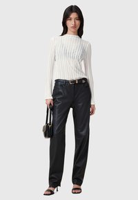 Top a maniche lunghe a righe bianche con collo alto abbinato a pantaloni in pelle nera e sandali neri con tacco. Include una piccola borsa nera.