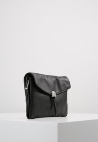 Czarna skórzana torba o teksturowanej powierzchni, z klapą na złożeniu i zapięciem w srebrnym odcieniu. Posiada prostokątny kształt i opływowy design.