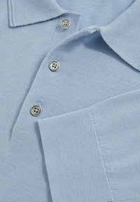 Himmelblaues Polohemd aus strukturiertem Strickstoff, mit zwei silbernen Knöpfen und einer Brusttasche. Sauberes Design mit genähten Saumdetails.