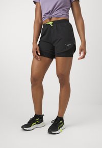 Shorts atletici negri cu elastic galben, având un buzunar lateral și detalii cu logo. Purtați cu adidași negri și verzi neon.