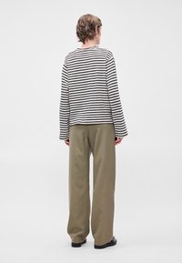 Camisola de manga longa às riscas em preto e branco com mangas largas, combinada com calças largas em verde-oliva e sapatos pretos.