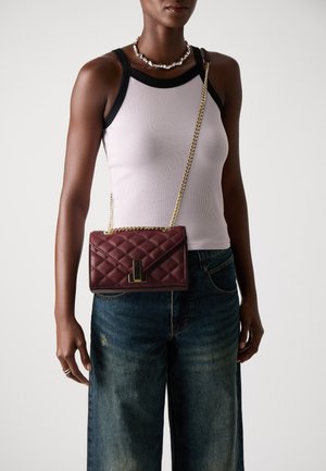 Sac bandoulière matelassé bordeaux avec une bandoulière en chaîne dorée et un fermoir rectangulaire, présentant un cuir lisse et une forme structurée.