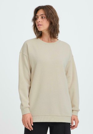 Beżowa bluza z długim rękawem, okrągłym dekoltem i ściągaczami. Miękka, fakturowana tkanina z luźnym krojem. Minimalistyczny design.